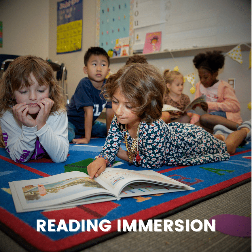 Two children sit on a rug, reading a book together
